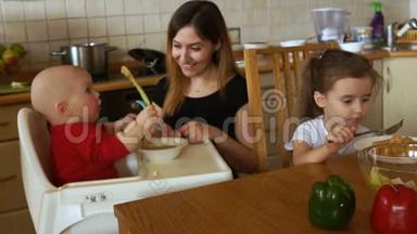 <strong>一个</strong>女人在厨房里喂两个孩子。 椅子上的孩子玩<strong>勺子</strong>，不想吃东西。 护士